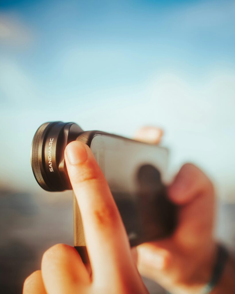 Hands holding a smartphone with an attached Sandmarc lens capturing an outdoor scene.